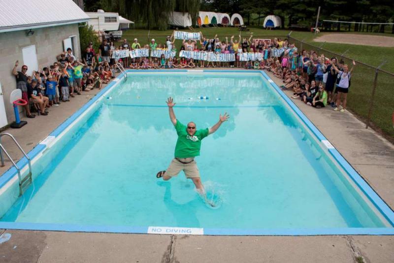 A man jumping in a swimming pool with many children watching 