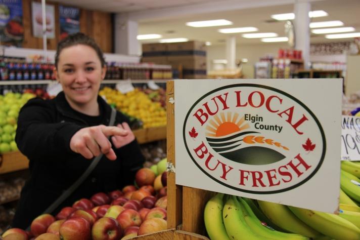 A woman pointing at Buy Local Buy Fresh Elgin County sign 